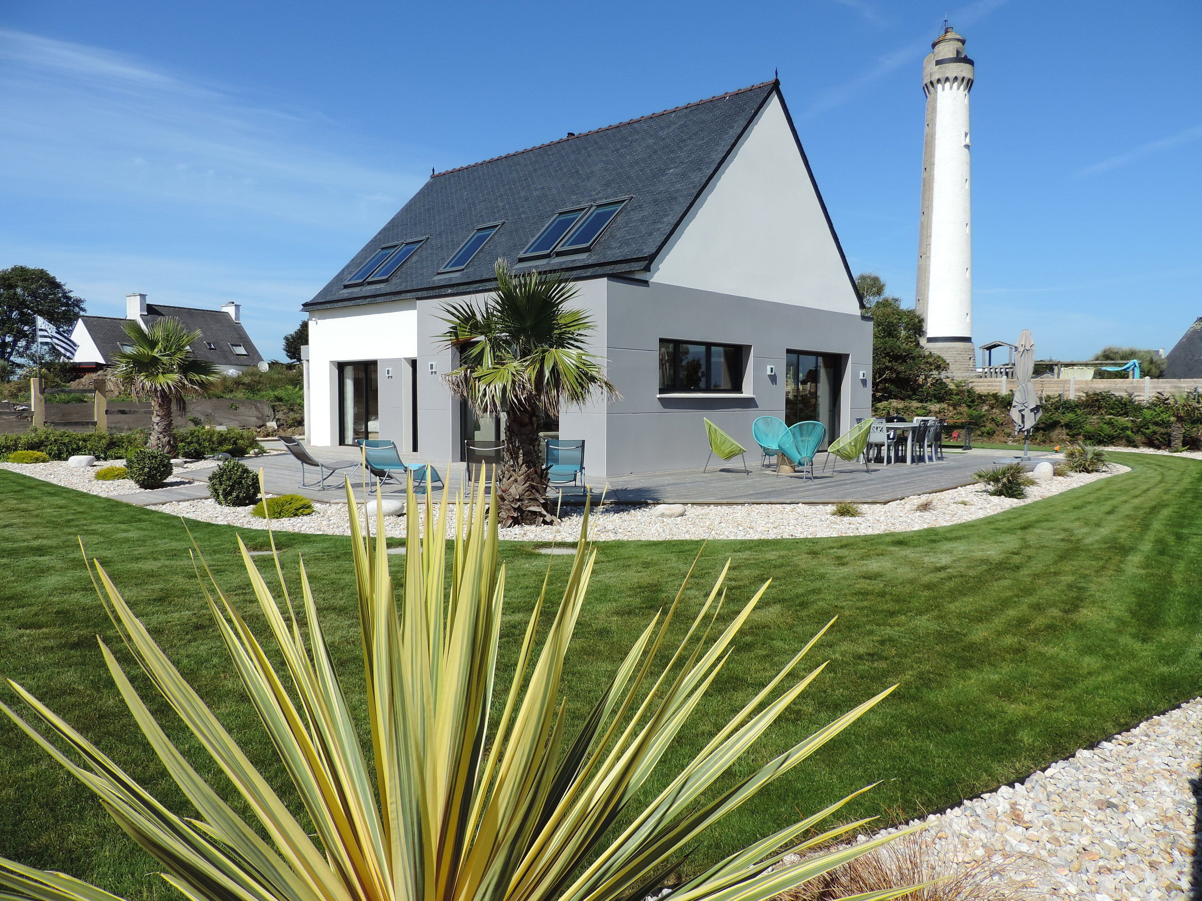 Una casa moderna con techo inclinado, paneles solares y un patio con sillas.