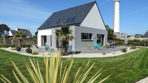 Une maison moderne avec un toit en pente, des panneaux solaires et une terrasse équipée de chaises.