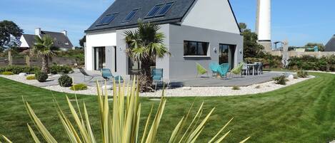 A modern house with a sloped roof, solar panels, and a patio with chairs.