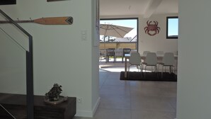 Un intérieur moderne avec un escalier, un coin repas comprenant des chaises et une table, et une grande fenêtre avec un parasol.