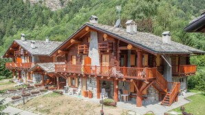 A large log cabin with multiple balconies and a stone foundation, surrounded by lush greenery and a mountainous backdrop. - Belvilla by OYO Grbe Trilo Max (Antey-Saint-Andre)