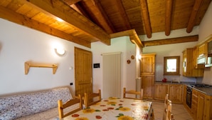 A cozy room with a wooden ceiling, a sofa, a dining table with a floral tablecloth, wooden cabinets, and a kitchen area. - Belvilla by OYO Grbe Trilo Max (Antey-Saint-Andre)