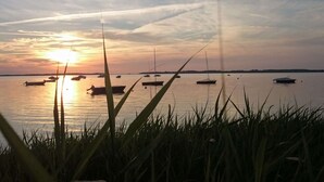 Solnedgang over et roligt vandareal med flere både forankret, omgivet af græsarealer.