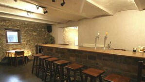 A bar area with a stone wall, wooden stools, a bar counter, and a window. - Grand Family Farmhouse in Anthisnes (Anthisnes)
