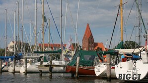 A marina with multiple boats docked, a church in the background, and a clear sky.