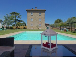 A swimming pool with a stone building in the background, a glass table with a lantern, and outdoor furniture. - Belvilla by OYO Villa Paola (Cortona)