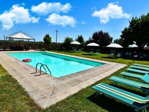 Ein rechteckiger Pool mit Sprungbrett, umgeben von einer Rasenfläche mit Liegestühlen und Sonnenschirmen.