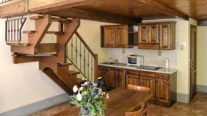 Un escalier en bois mène à une cuisine dotée de meubles en bois et à une table à manger ornée d’un vase de fleurs.