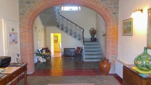 Un vaste espace de vie agrémenté d’une arche en pierre menant à un escalier, d’un grand vase et d’un tapis sur le sol.