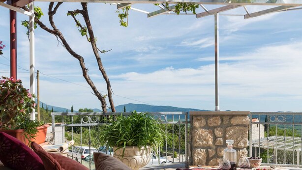 Eine Terrasse mit Steinmauer, einem Holztisch, der mit Speisen gedeckt ist, und Blick auf die Landschaft.