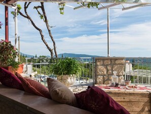 Une terrasse avec un mur en pierre, une table en bois dressée pour le repas, et une vue sur le paysage.