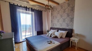 Ein Schlafzimmer mit einem großen Bett, einem Nachttisch, einer Kommode und Blick ins Freie.