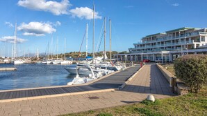 A marina with multiple sailboats docked, a paved walkway, and a modern building with balconies. - Apartment With Terrace for 4 People (Olbia)