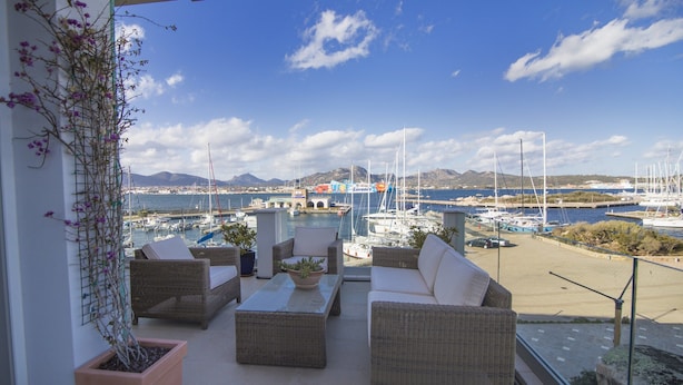 A balcony with wicker furniture, potted plants, and a view of a marina with boats and mountains in the background. - Apartment With Terrace for 4 People (Olbia)