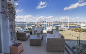 A balcony with wicker furniture, potted plants, and a view of a marina with boats and mountains in the background. - Apartment With Terrace for 4 People (Olbia)