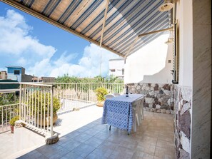 A covered outdoor patio with a table and chairs, a bottle of wine, and a stone wall.