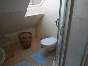 A small bathroom with a toilet, a shower, a window, and a wicker basket. - Kinderparadies - Ferienwohnung mit Garten (Blowatz)