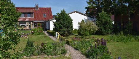 Een woonwijk met een verhard pad, een tuin met diverse planten en een huis met een rood dak.