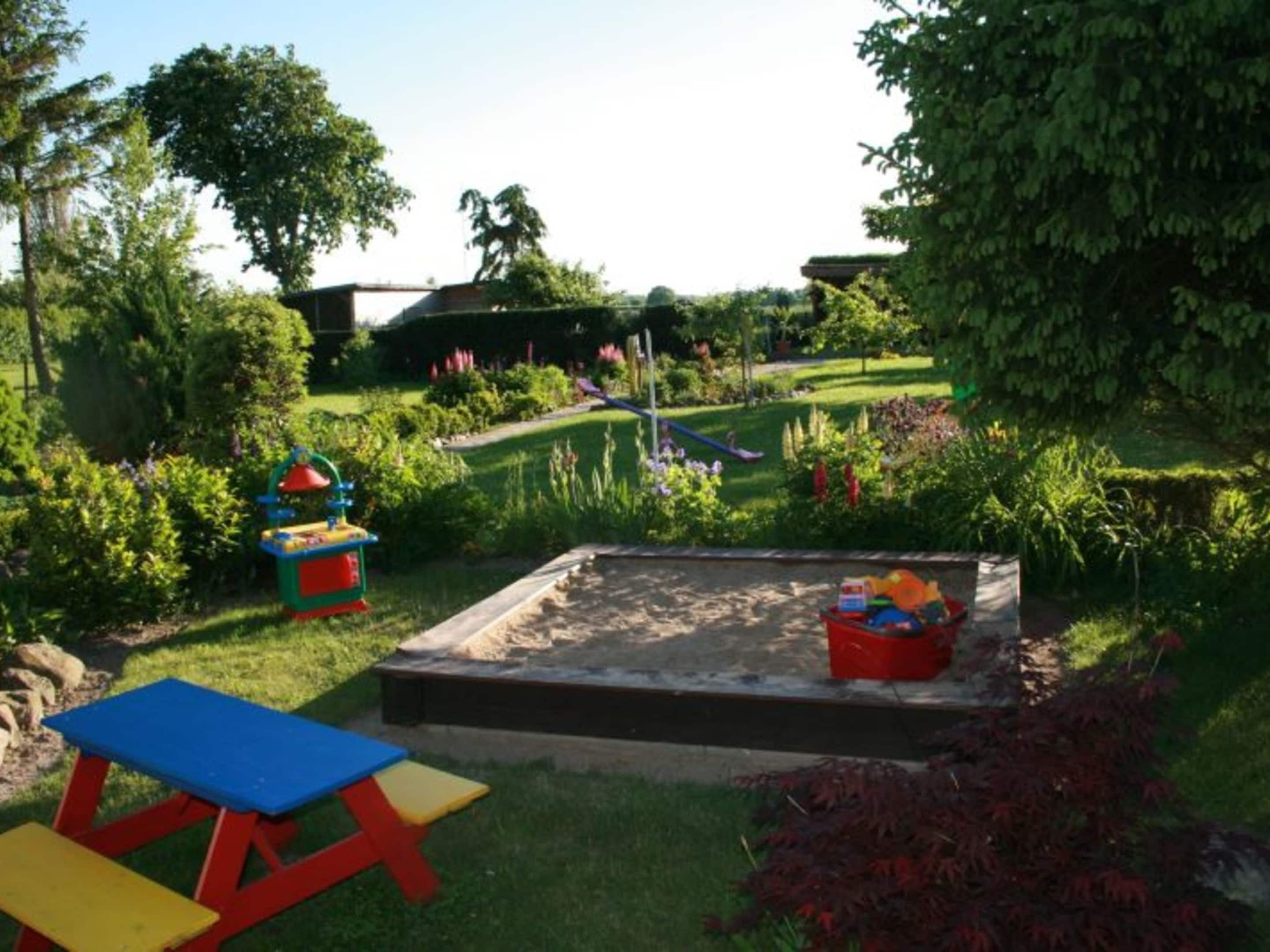 A garden with a sandbox, a slide, and a picnic table.