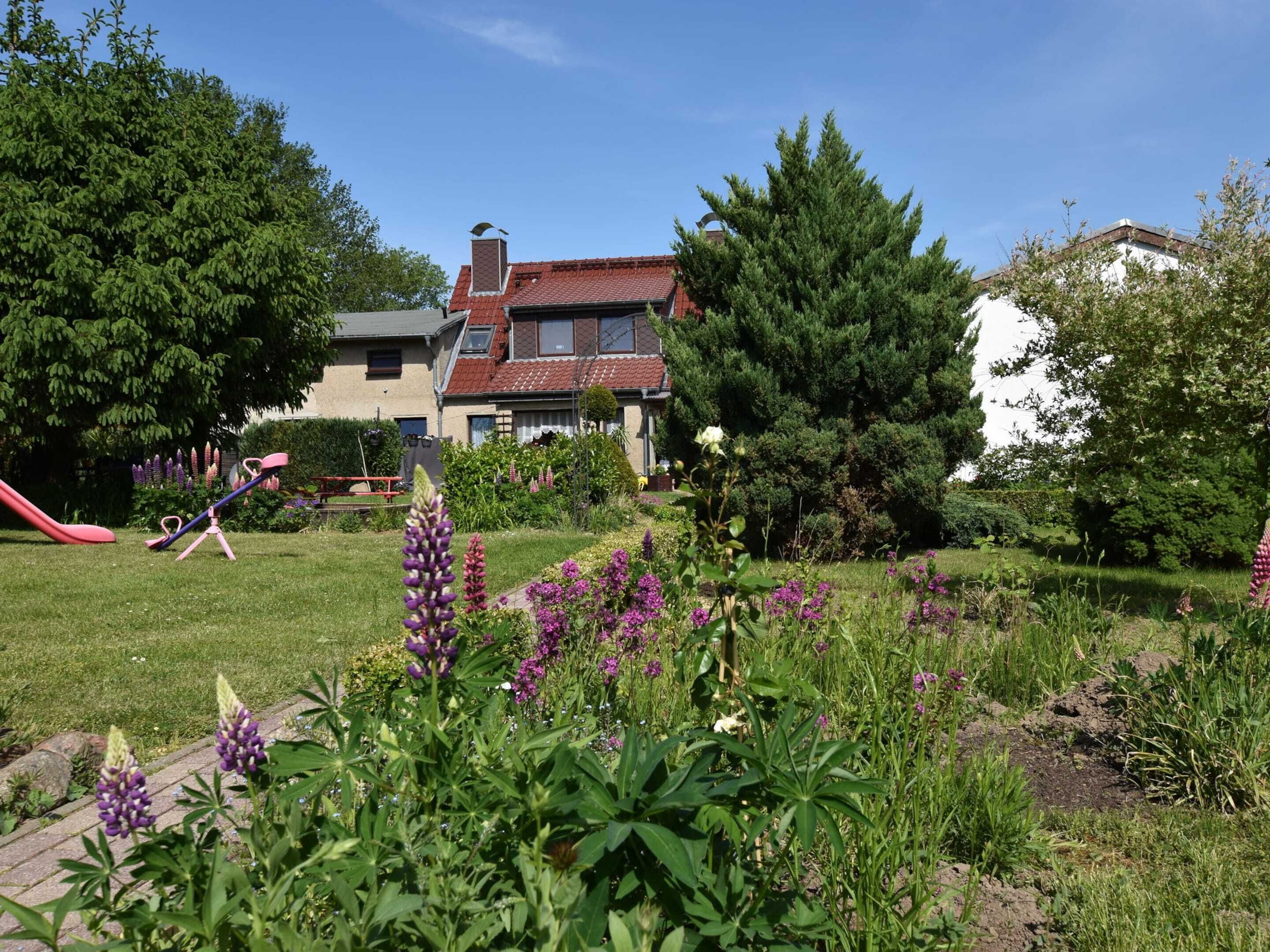 A residential garden with a red slide, a swing set, and various flowering plants.