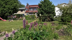 A residential garden with a red slide, a swing set, and various flowering plants. - Kinderparadies - Ferienwohnung mit Garten (Blowatz)
