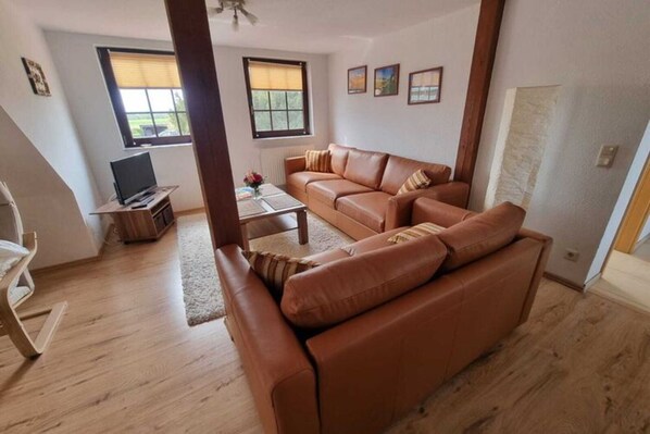 A living room with a brown leather sofa, a wooden coffee table, and a television on a stand. - Kinderparadies - Ferienwohnung mit Garten (Blowatz)