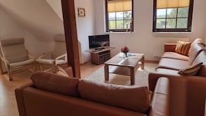 A living room with a brown leather sofa, a wooden coffee table, a TV, and two windows with blinds. - Kinderparadies - Ferienwohnung mit Garten (Blowatz)