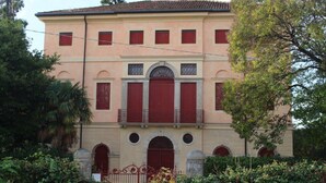 A two-story building with a symmetrical facade, red shutters, and a central arched window. - Venice Region Castle With Garden Views (Romano d'Ezzelino)