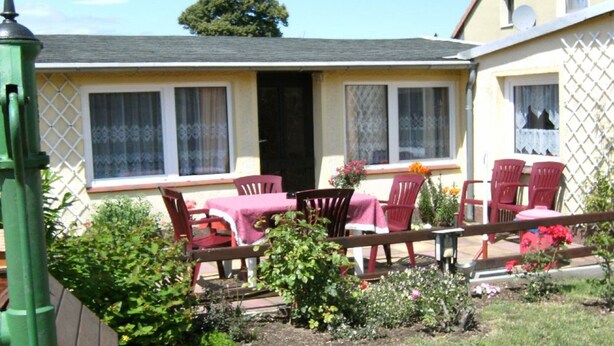 A small house with a patio area featuring a table and chairs, surrounded by a garden with various plants and flowers. - Bungalow in Zweedorf, Ostsee (Bastorf)