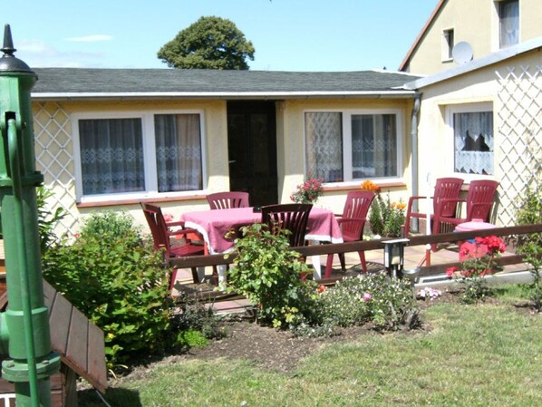 A small house with a patio area featuring a table and chairs, surrounded by a garden with various plants and flowers. - Bungalow in Zweedorf, Ostsee (Bastorf)