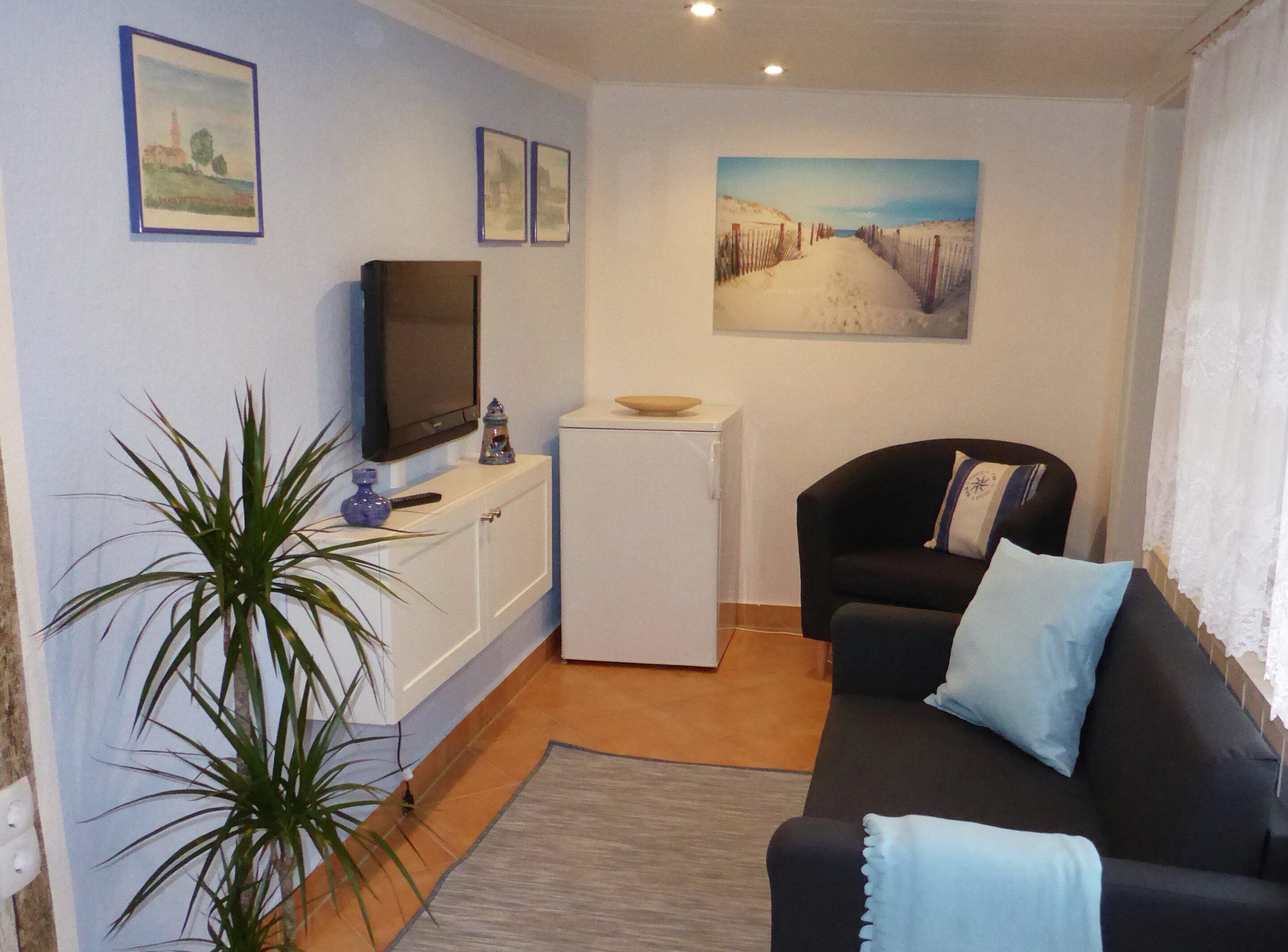 Una sala de estar con un sofá negro, un mueble blanco pequeño, un televisor y un cuadro en la pared.