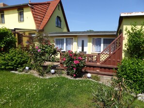 A yellow house with a red roof, a wooden deck, and a garden with pink flowers. - Bungalow in Zweedorf, Ostsee (Bastorf)