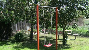 A swing set in a grassy area with a fence and trees in the background. - Bungalow in Zweedorf, Ostsee (Bastorf)