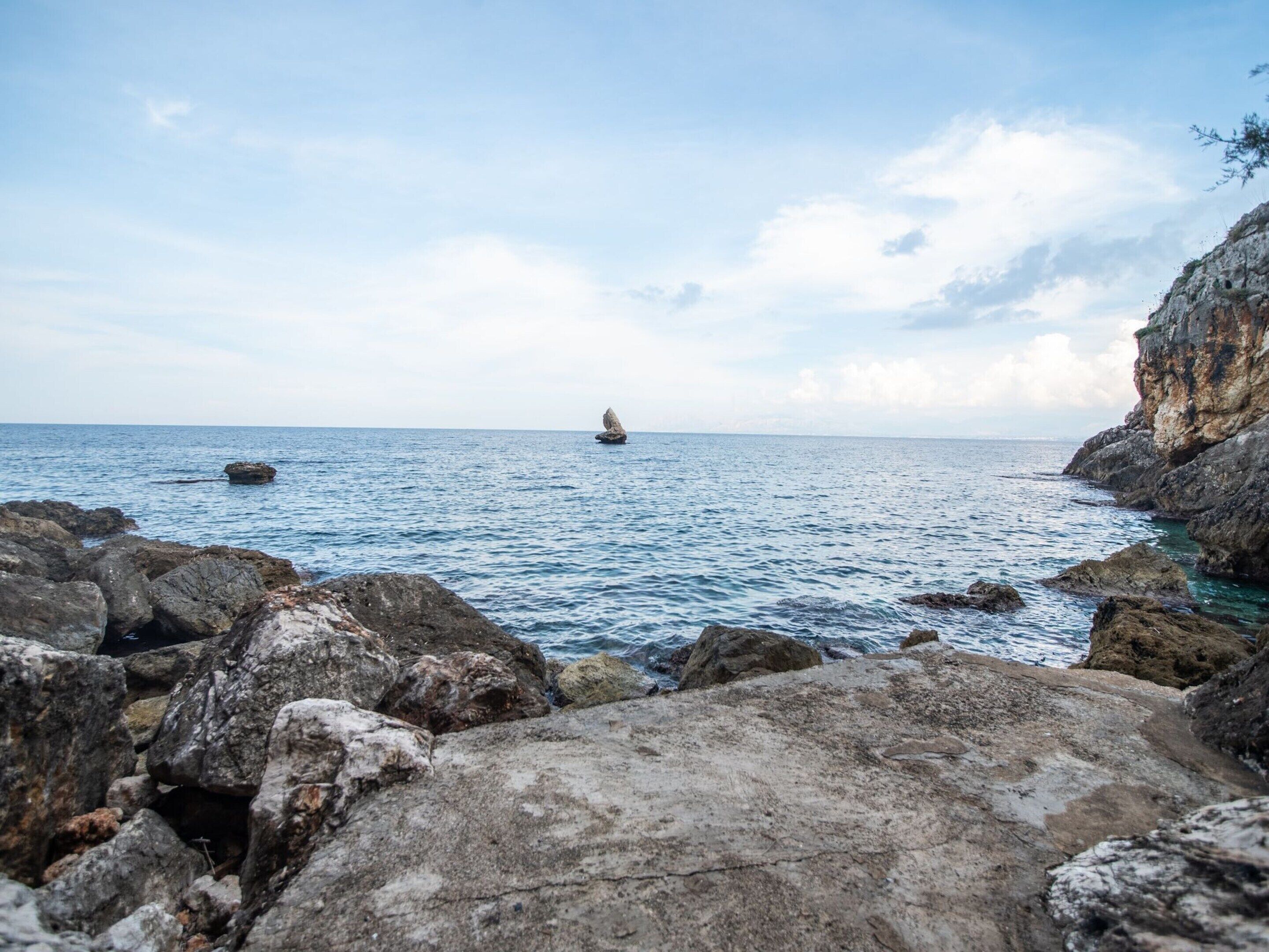 A rocky coastline with clear blue sea and distant land.