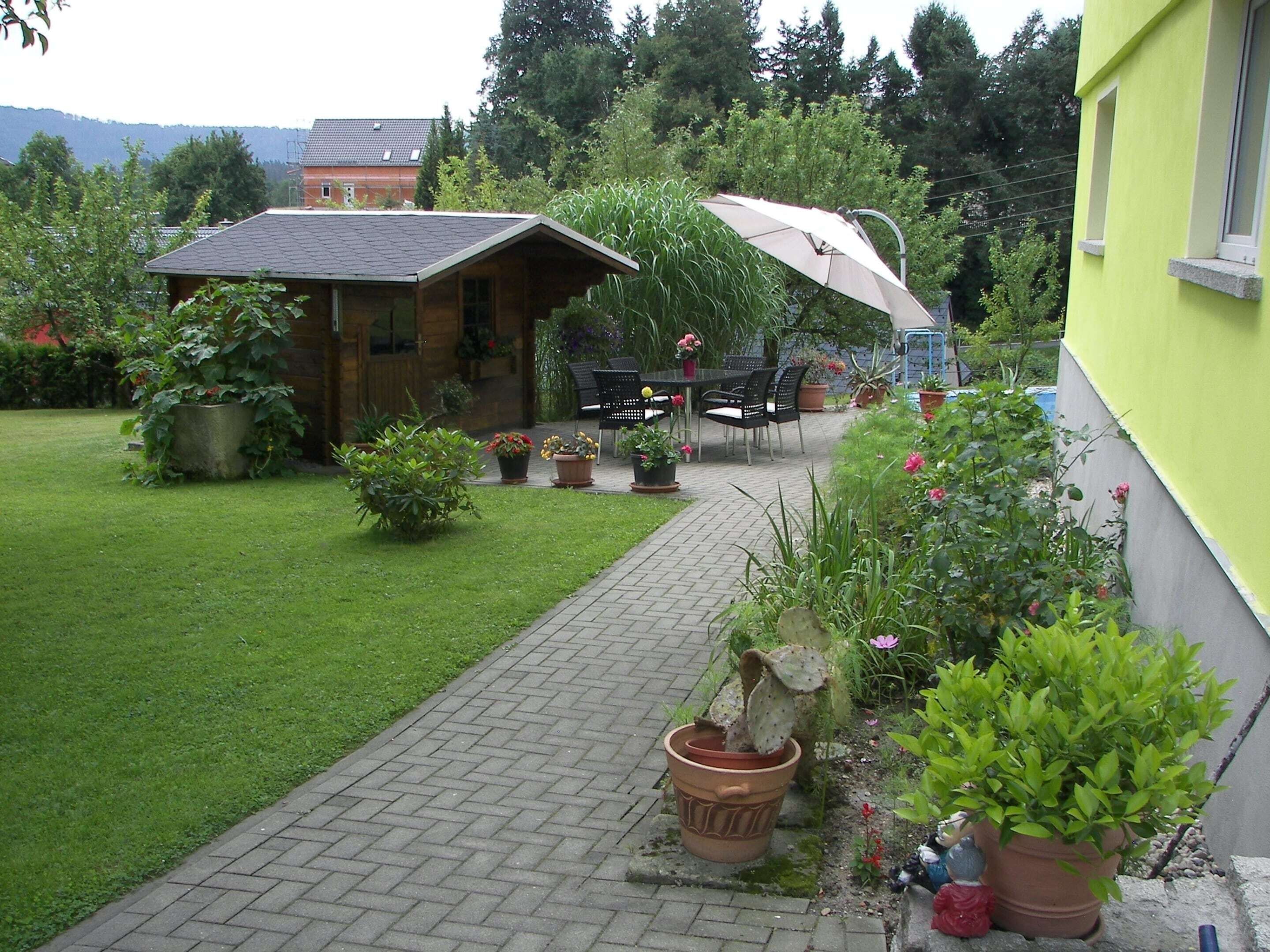 A garden with a patio area, potted plants, and a wooden building.