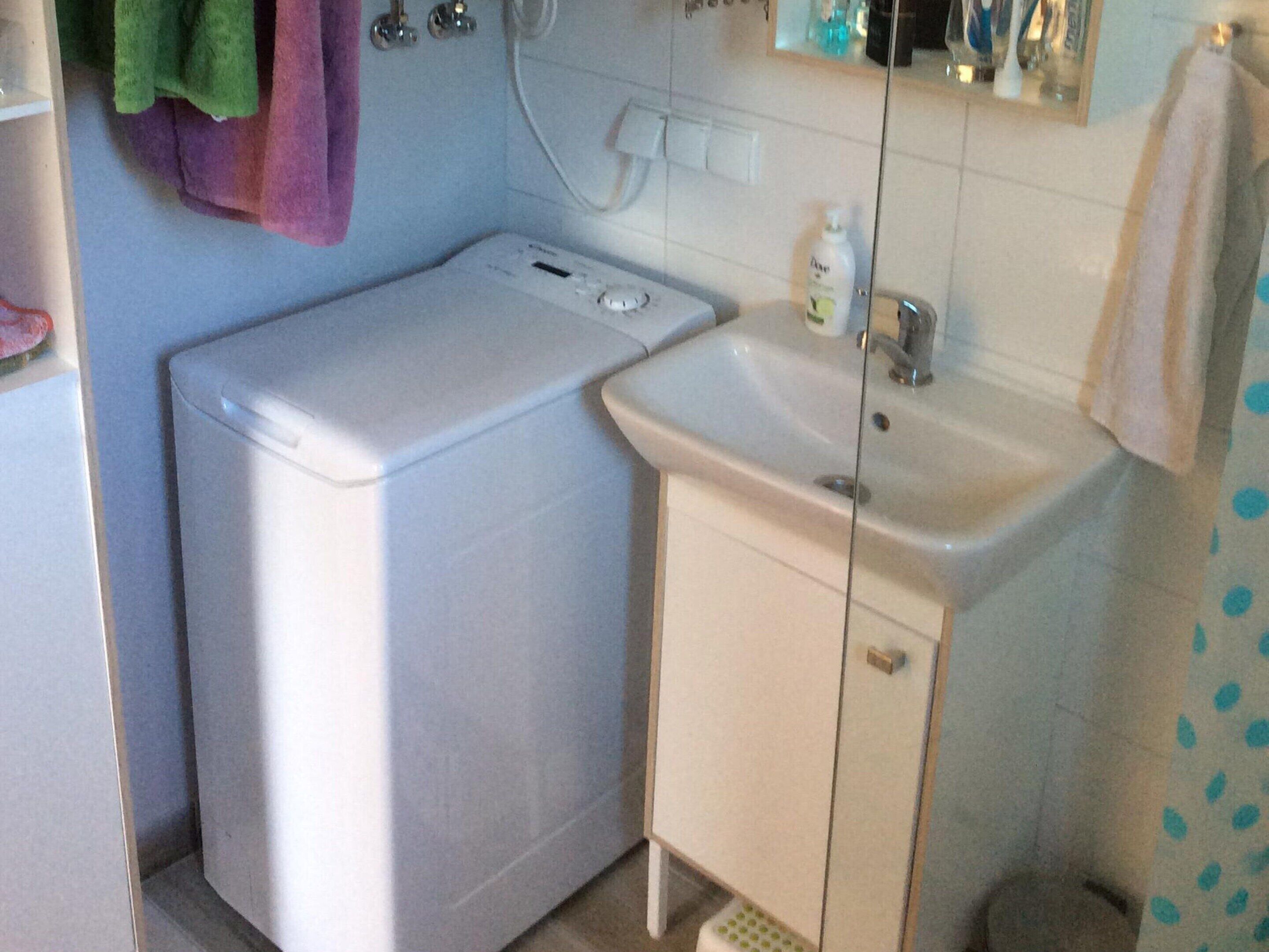 Ein kleines Badezimmer mit Waschmaschine, Waschbecken und Spiegel.