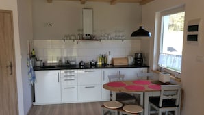 A kitchen with white cabinets, a black countertop, and a window with a view of trees. There is a dining table with pink placemats and two chairs.