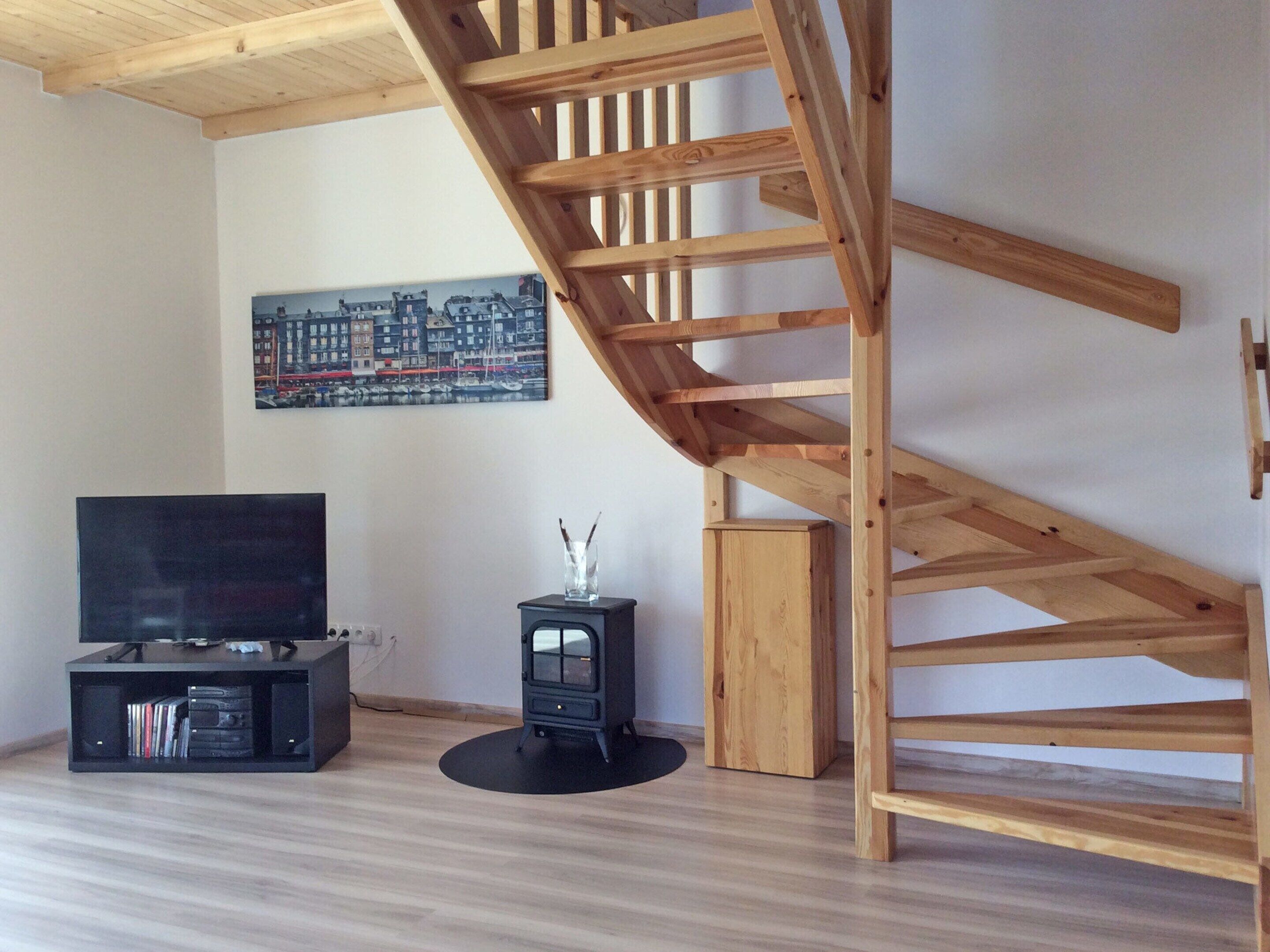 A living room with a wooden staircase, a black entertainment unit, and a painting of a cityscape.