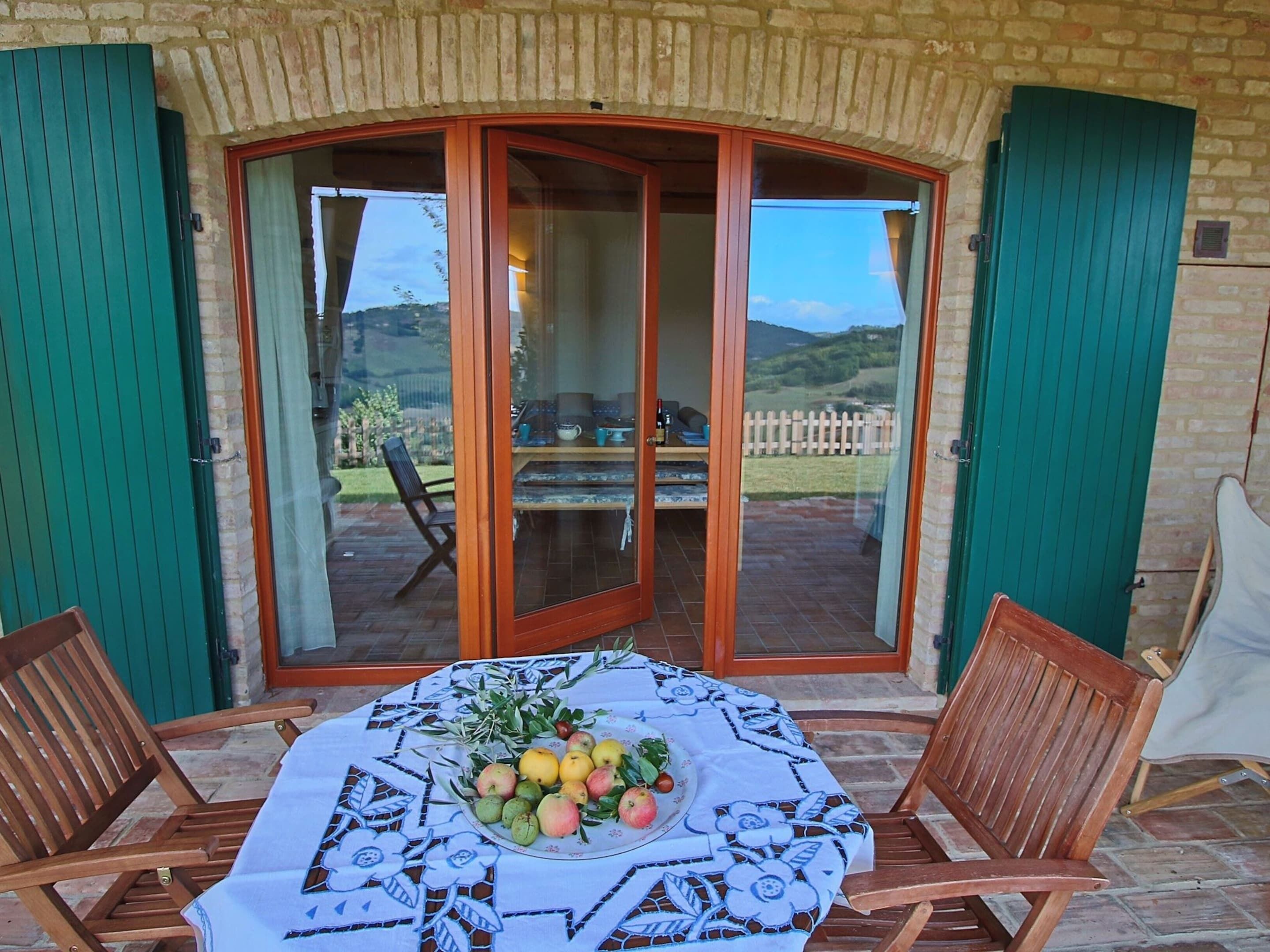 A patio with a table set for dining, featuring a fruit bowl and a tablecloth.