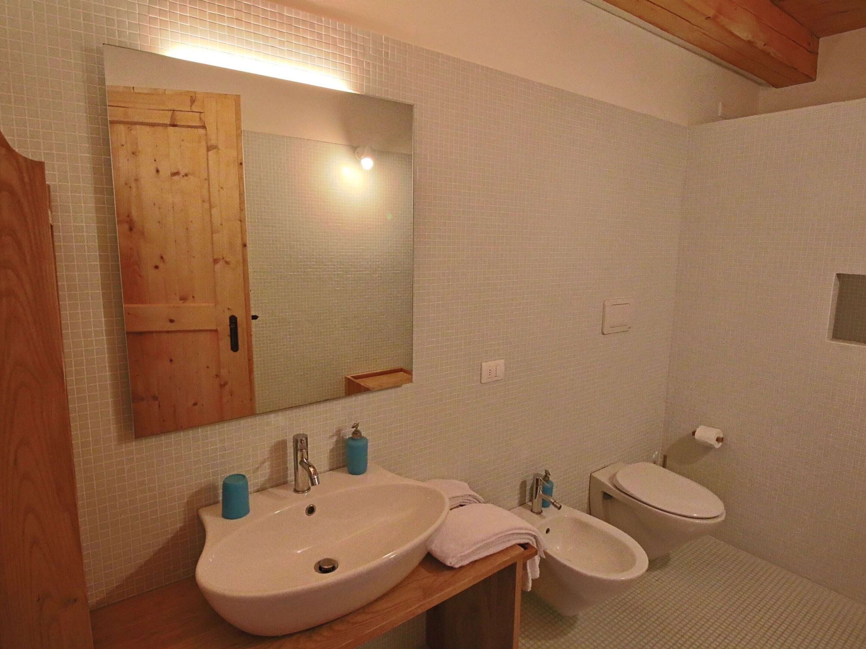 Un bagno con porta in legno, lavandino, bidet e specchio.