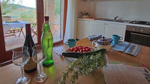 A kitchen with a view of the outdoors, a table with wine bottles, glasses, a bowl of cherries, and a sprig of rosemary. - Tranquil Hilltop Cottage (Montelabbate)
