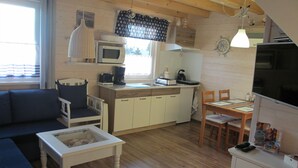 Une chambre confortable, aménagée dans le style d’un chalet, avec un plancher en bois, un canapé, une table à manger, un coin cuisine équipé d’un four à micro-ondes et un téléviseur.