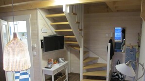 Un espace de vie compact comprenant un escalier, un téléviseur fixé au mur, un petit bureau avec un panier et un luminaire suspendu.