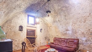 A cozy attic room with a rustic stone wall, a brown leather sofa, a wicker rocking chair, a wooden coffee table, and a small wooden chest. - Holiday Home in Stilo With Pool & Views (Stilo)
