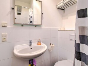 A bathroom with a white sink, a mirror, a towel rack, a toilet, and a glass shelf above the sink. - Wohnung in Wismar mit Eigener Terrasse (Wismar)
