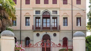 A building with a symmetrical facade, multiple windows, and a central entrance with a decorative gate. - Castle in Romano D'ezzelino With Garden (Romano d'Ezzelino)