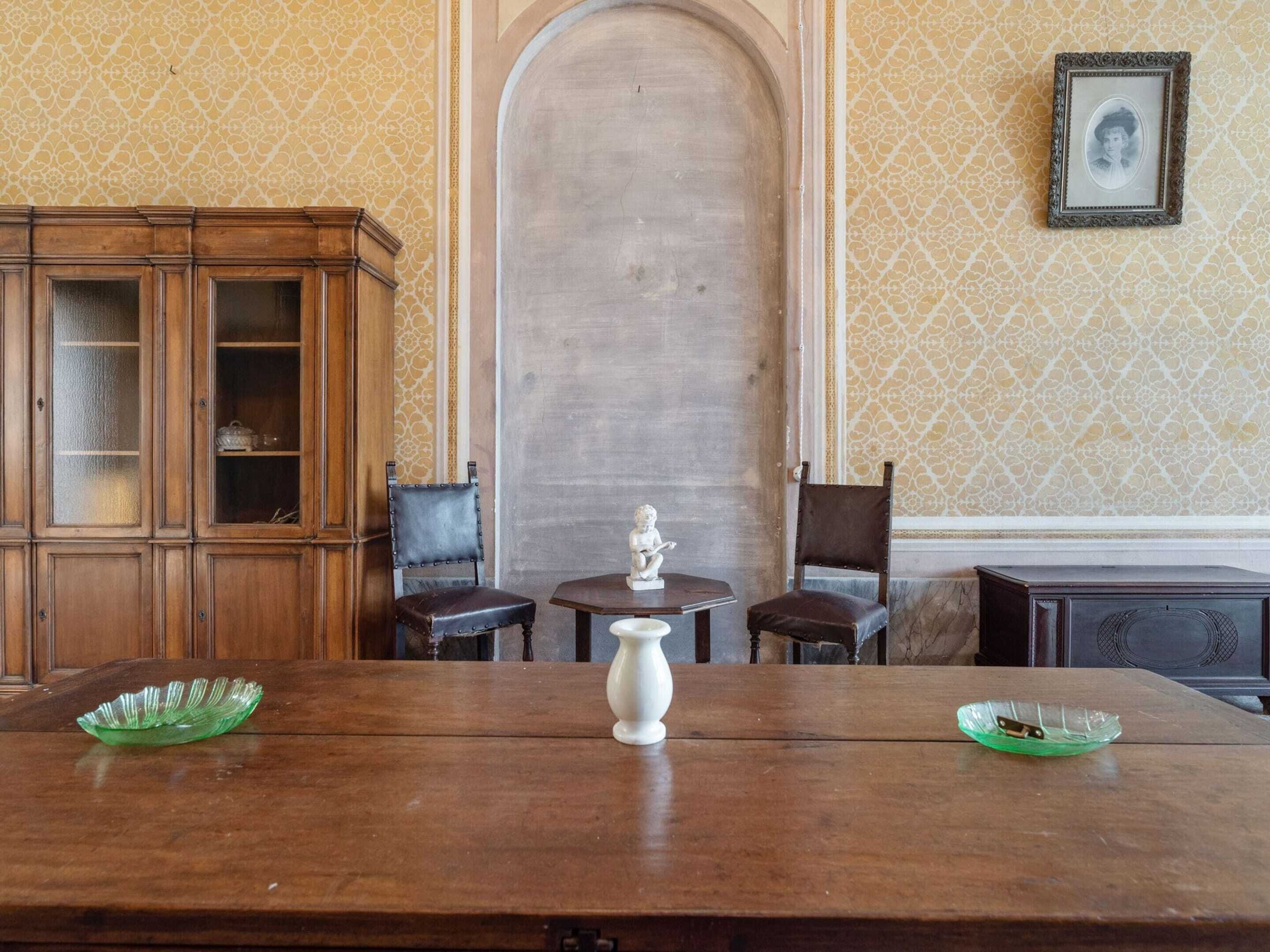 A room with a wooden table, two chairs, a cabinet, and a wall-mounted picture frame.