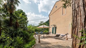 A patio area with a table and chairs, surrounded by lush greenery and a large tree. - Castle in Romano D'ezzelino With Garden (Romano d'Ezzelino)