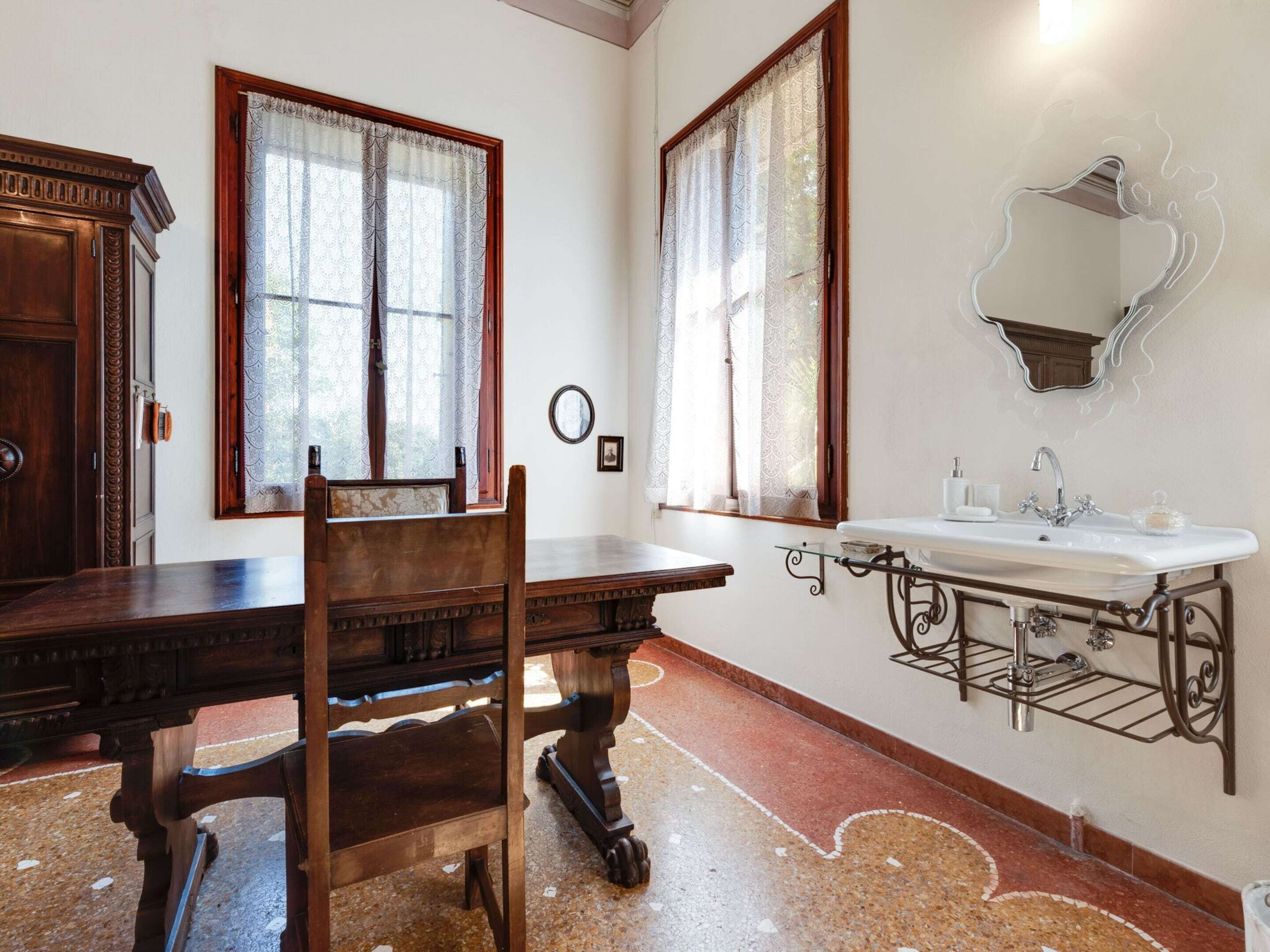 A room with a wooden dining table, chairs, a large mirror, and a white sink with a metal frame.