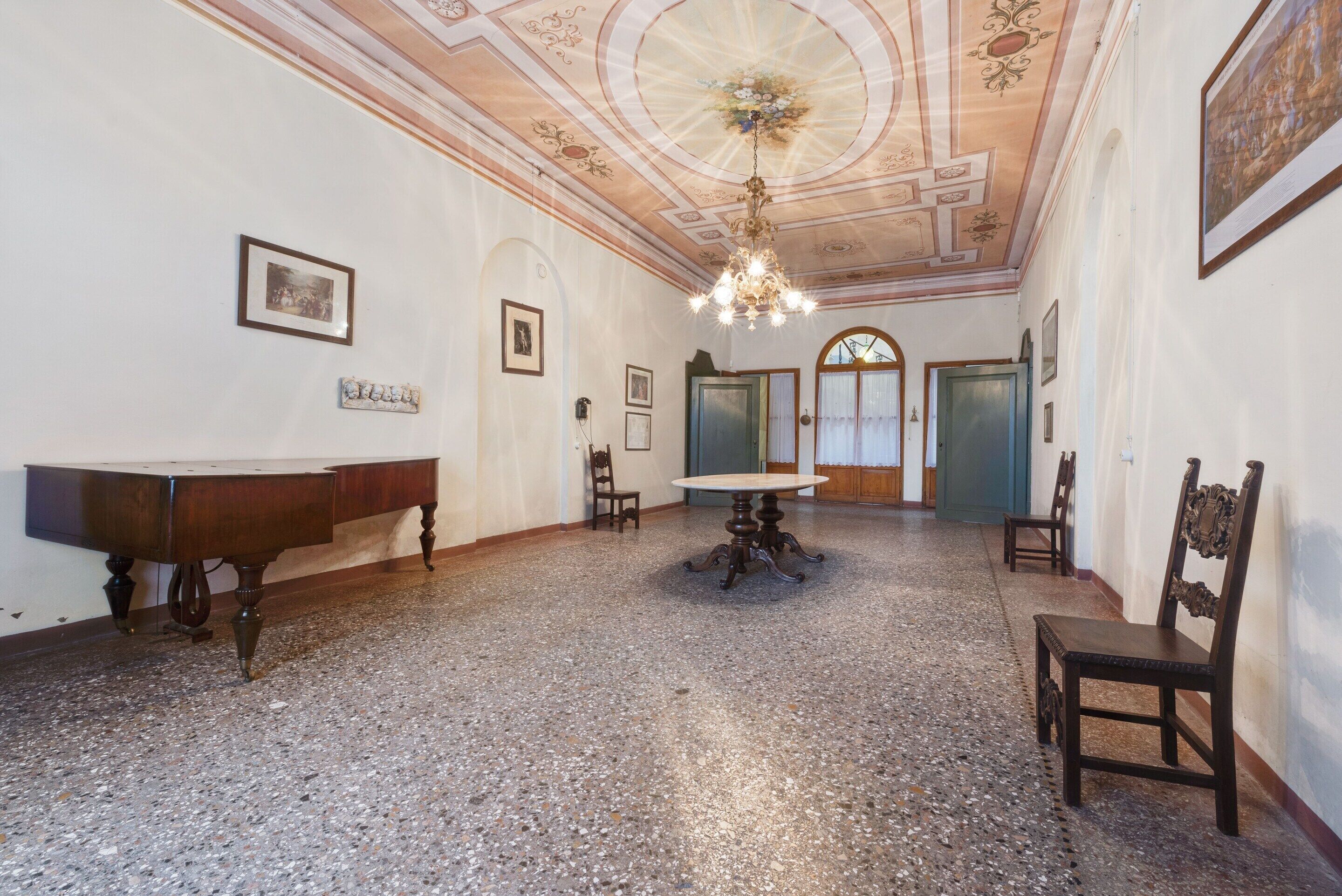 Un'ampia stanza con un pavimento in terrazzo lucido, un tavolo di legno con sedie e un lampadario.